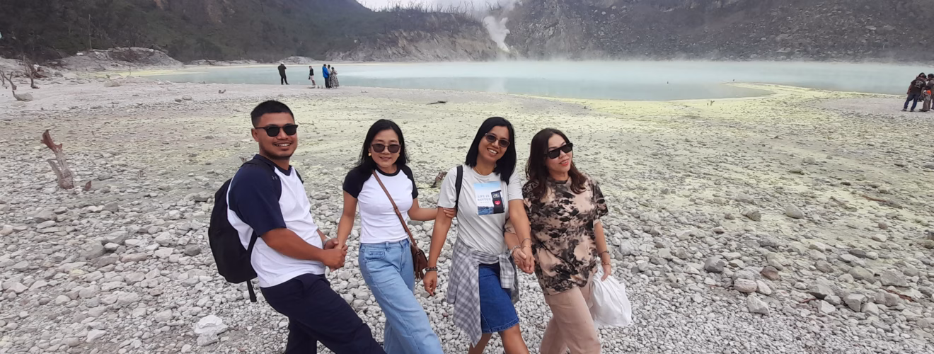 A group of travelers posing by the turquoise crater lake at Kawah Putih, Ciwidey, West Java, surrounded by misty hills.
