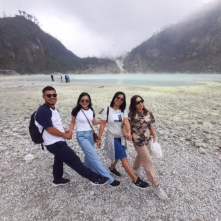 A group of travelers posing by the turquoise crater lake at Kawah Putih, Ciwidey, West Java, surrounded by misty hills.