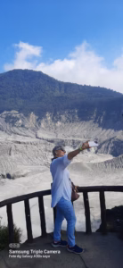 Wisatawan berfoto di gardu pandang dengan latar kawah gunung berapi dan dinding batu vulkanik.