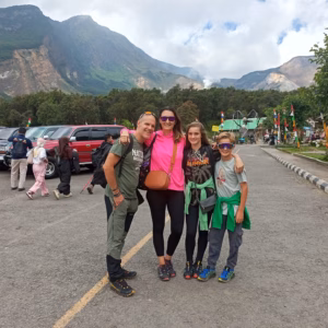 Keluarga wisata berfoto di area parkir Gunung Papandayan dengan latar pegunungan hijau dan kawah aktif.
