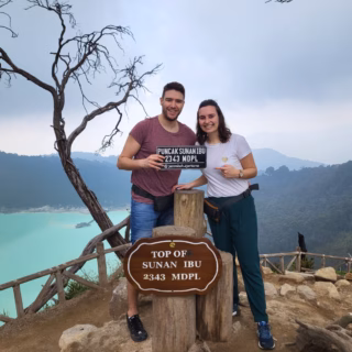 Dua wisatawan berfoto di puncak Sunan Ibu 2343 mdpl dengan latar danau kawah dan pegunungan.